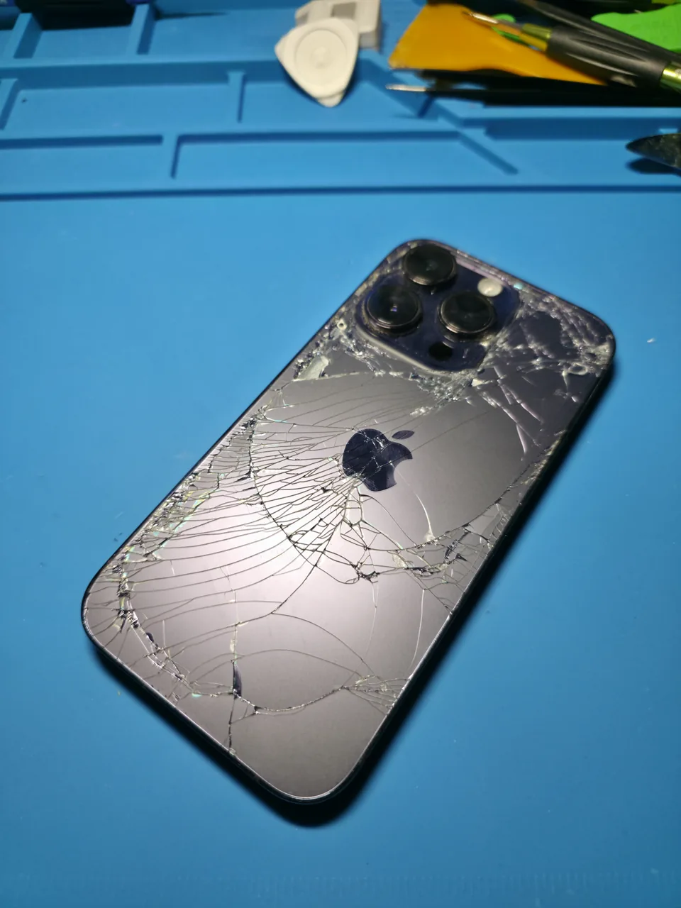 iPhone mit gesprungenem Rückglas auf einer blauen Reparaturmatte